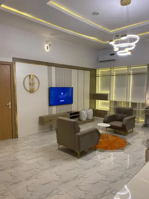 Lounge with a wall mounted TV and grey armchairs on marble flooring